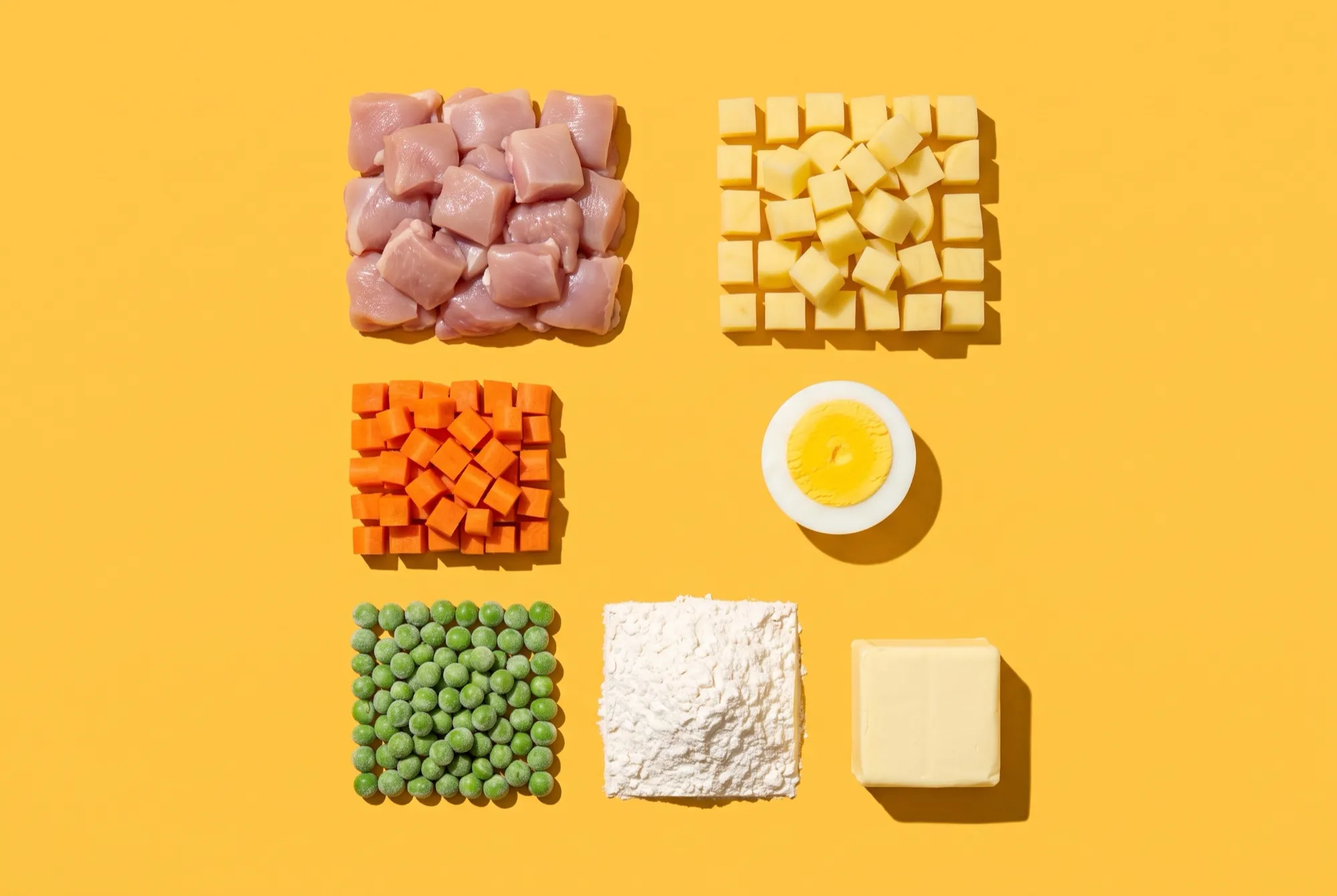 The filling ingredients laid out in neat squares: diced chicken thigh, potato cubes, diced carrot, green peas, half a hard-boiled egg, flour and a block of butter